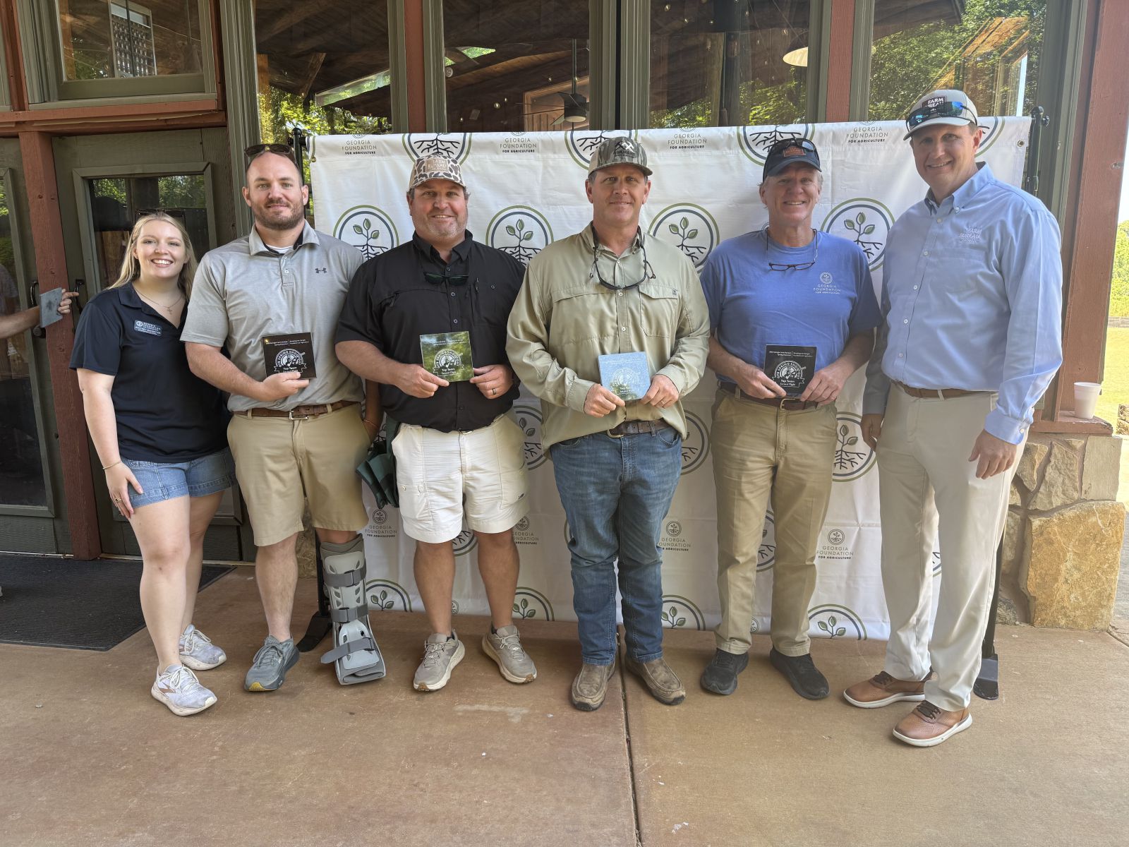 Four men in center hold small square granite plaques they are accepting from young lady on far left and tall man on far right.