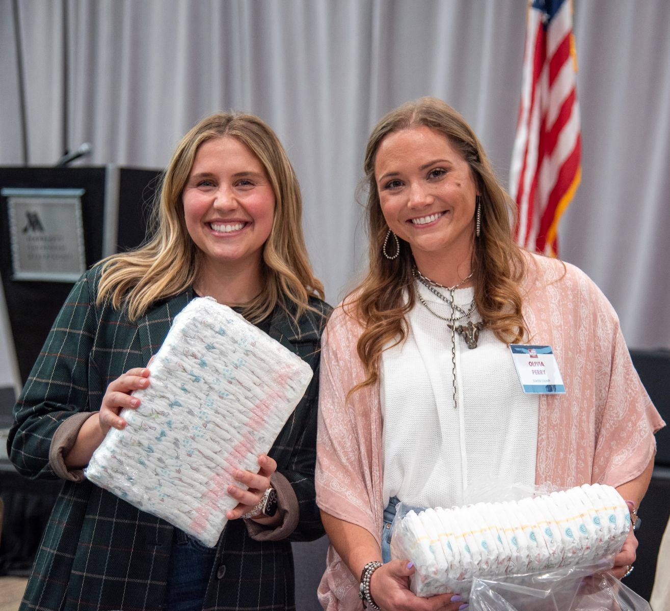 Two young smiling ladies hold diapers they are packing for a service project.