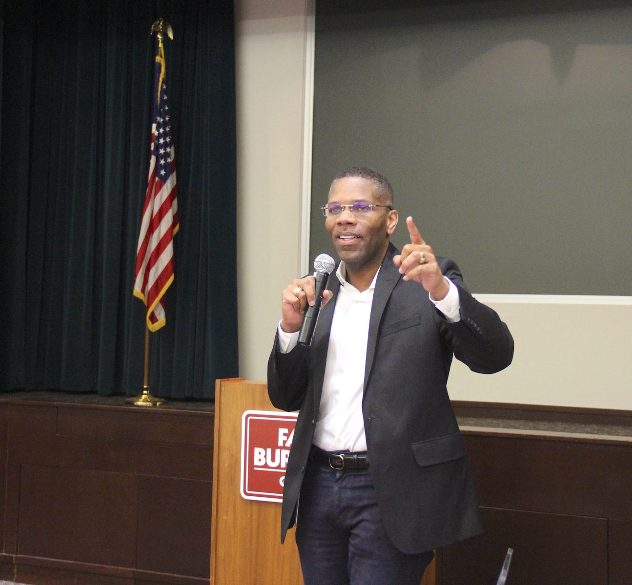 A man standing talks into a microphone with a U.S. flag in the background