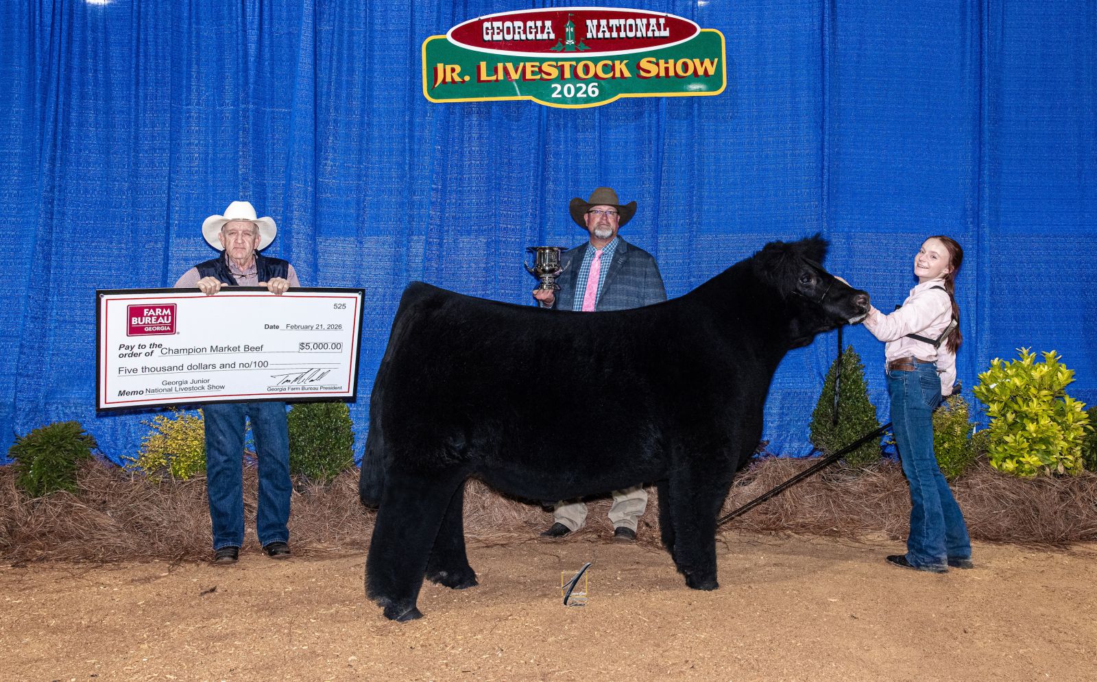 Teenage girl shows solid black beef steer as man on far left presents prize check and male show judge in middle presents trophy.