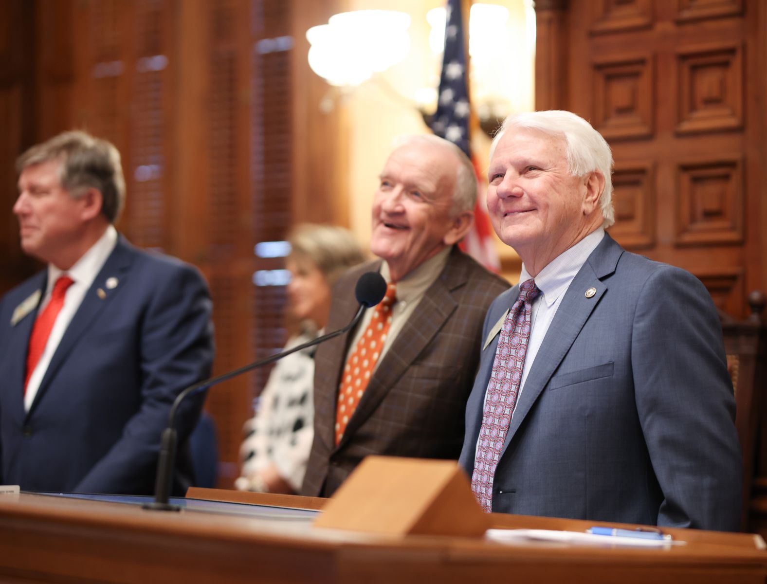 Three men wearing suits stand smiling in Georgia Capitol House Chamber.