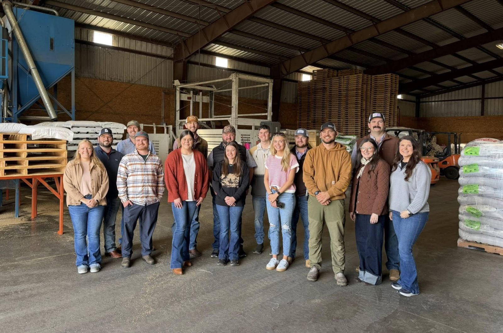 A group of 15 young people - six ladies nine guys dressed very casually - tour a seed warehouse.