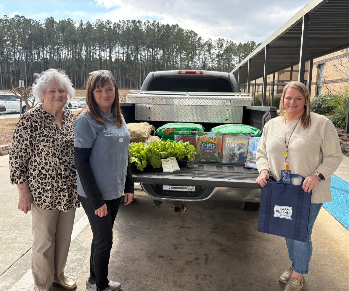 Three women around the tailgate of a pickup containing plants and farm-related books.