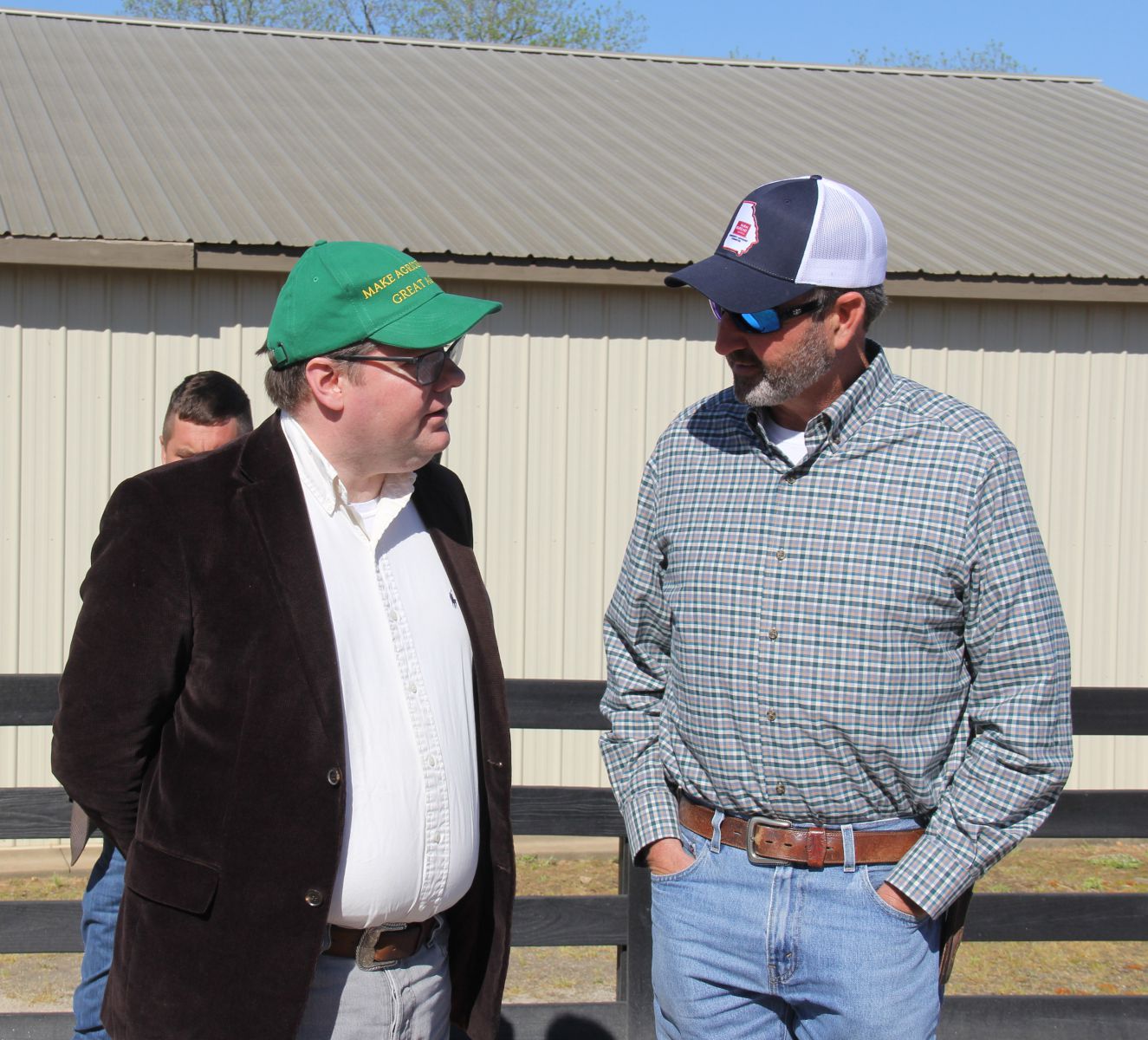 Two men standing in front of a black wooden fence talking.
